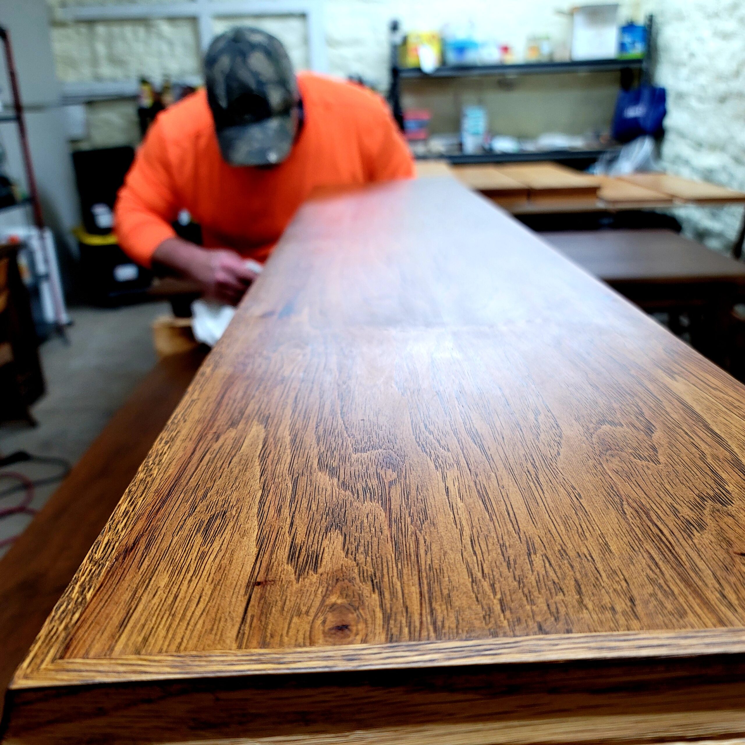 Craftsman applying finish to large wood surface in workshop.